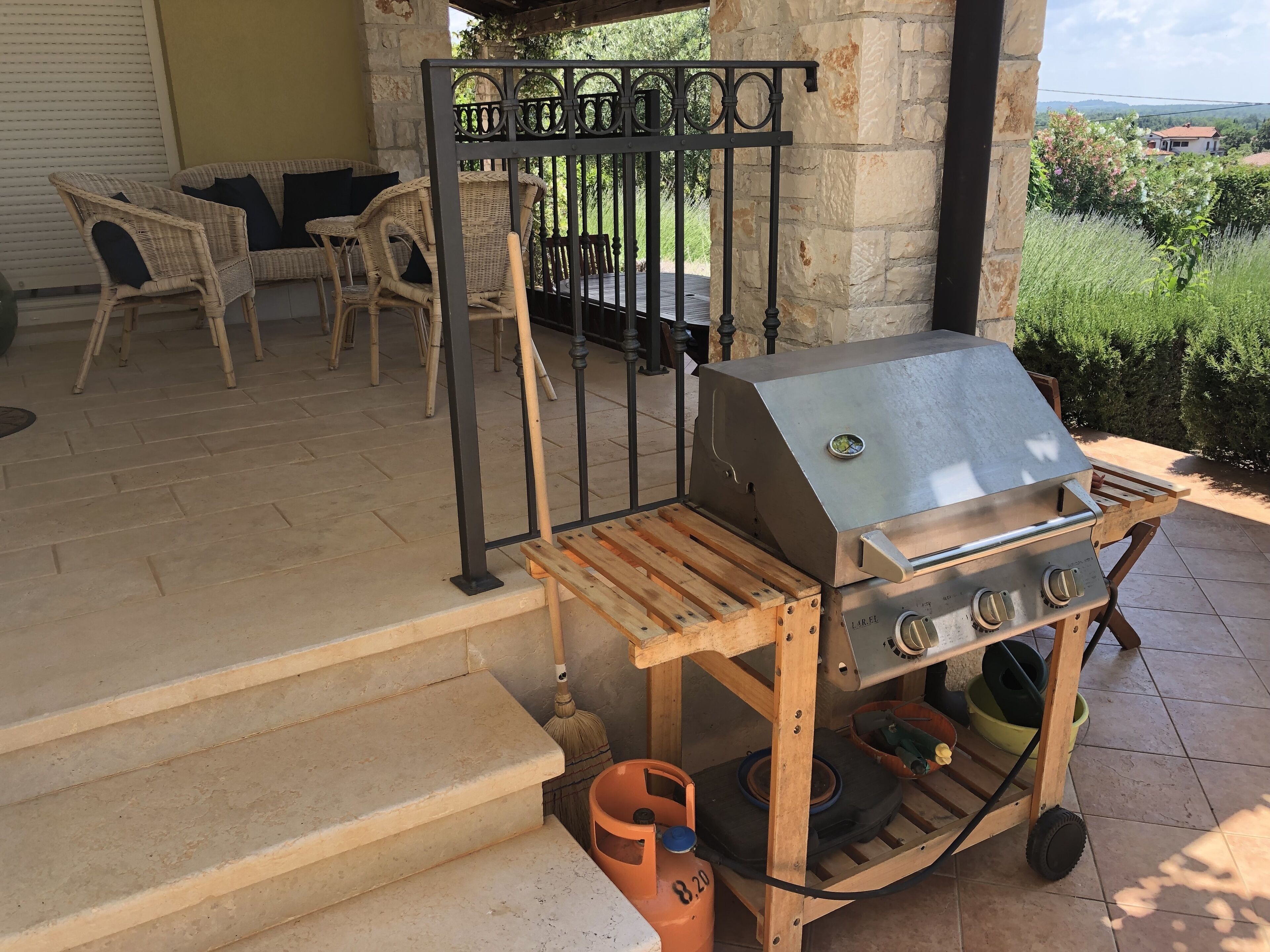 Une terrasse avec un barbecue, des meubles en osier et un mur en pierre.