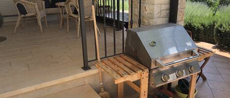 Une terrasse avec un barbecue, des meubles en osier et un mur en pierre.