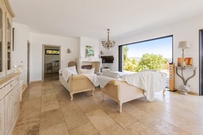 A spacious bedroom with two beds, a chandelier, a fireplace, and a large window with a view.