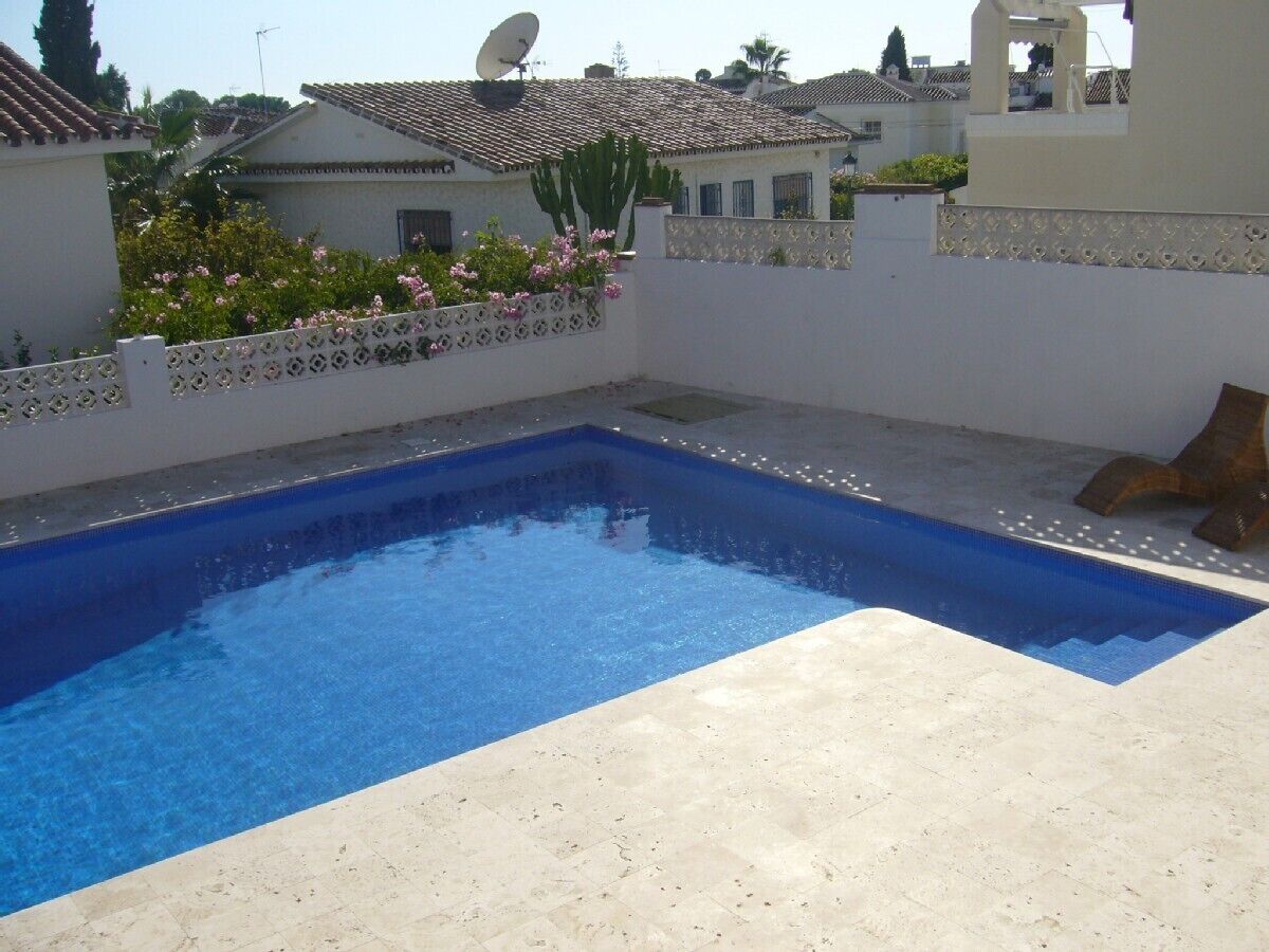 A rectangular swimming pool with a blue interior, surrounded by a white wall with decorative patterns.