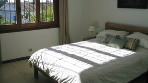 Ein Schlafzimmer mit Bett, Nachttisch, Lampe und einem Fenster mit Vorhängen.
