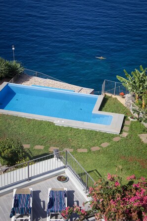 Ein Schwimmbecken mit Meerblick, eine Sonnenterrasse mit Liegestühlen und ein kleiner Gartenbereich.
