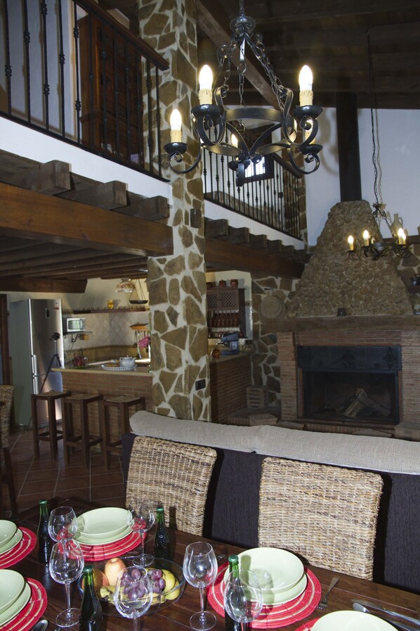 A dining area with a stone pillar, wicker chairs, a fireplace, and a chandelier.