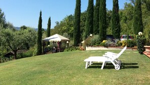 Une pelouse bien entretenue, agrémentée d’un fauteuil de jardin blanc, d’un belvédère et de grands cyprès en arrière-plan.