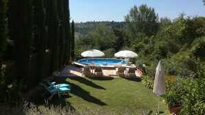Un jardin avec une piscine, deux parasols et des chaises longues.