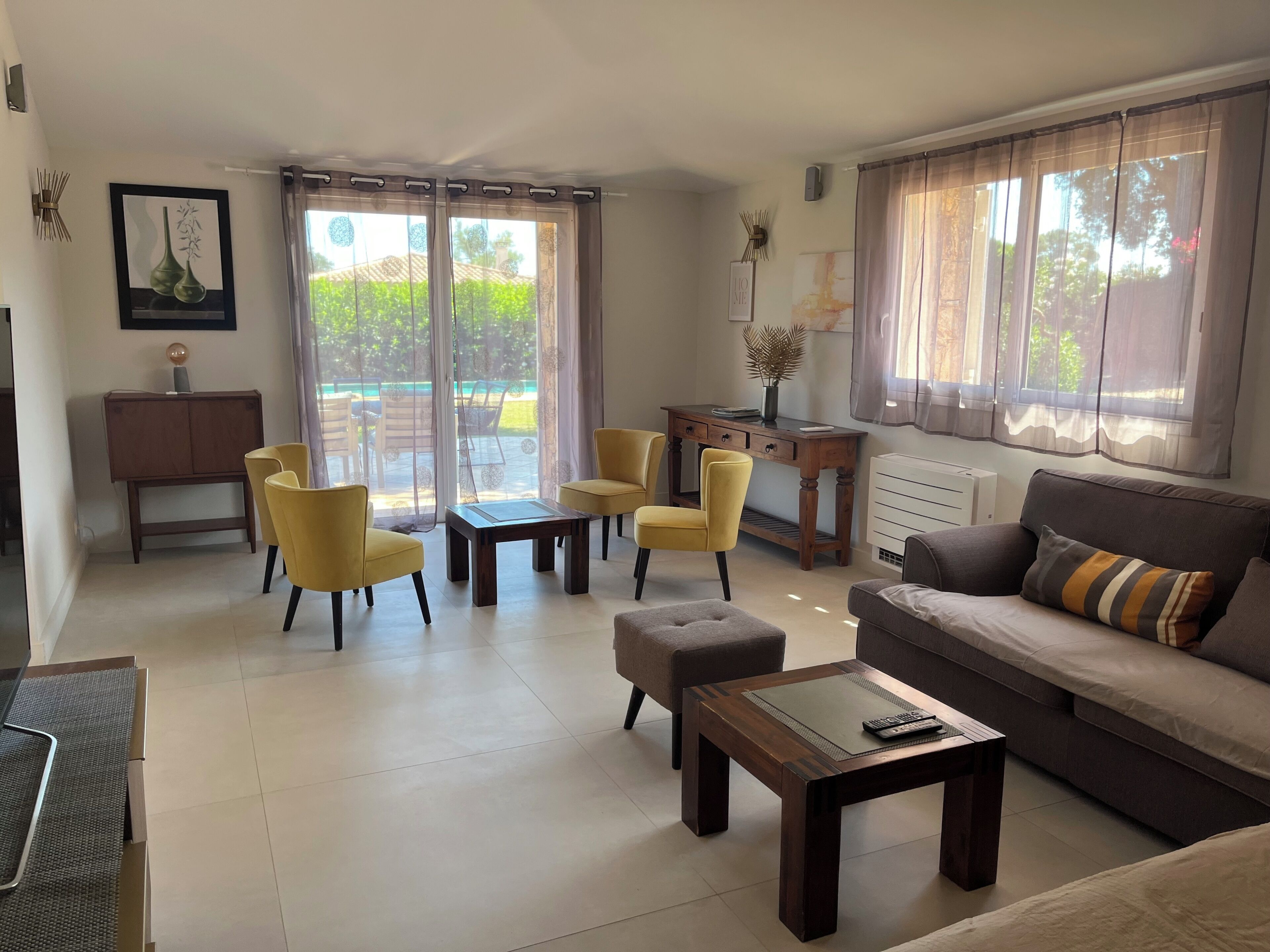 Un salon comprenant un canapé, deux fauteuils jaunes, une table basse, un bureau et une vue sur la verdure à l’extérieur.