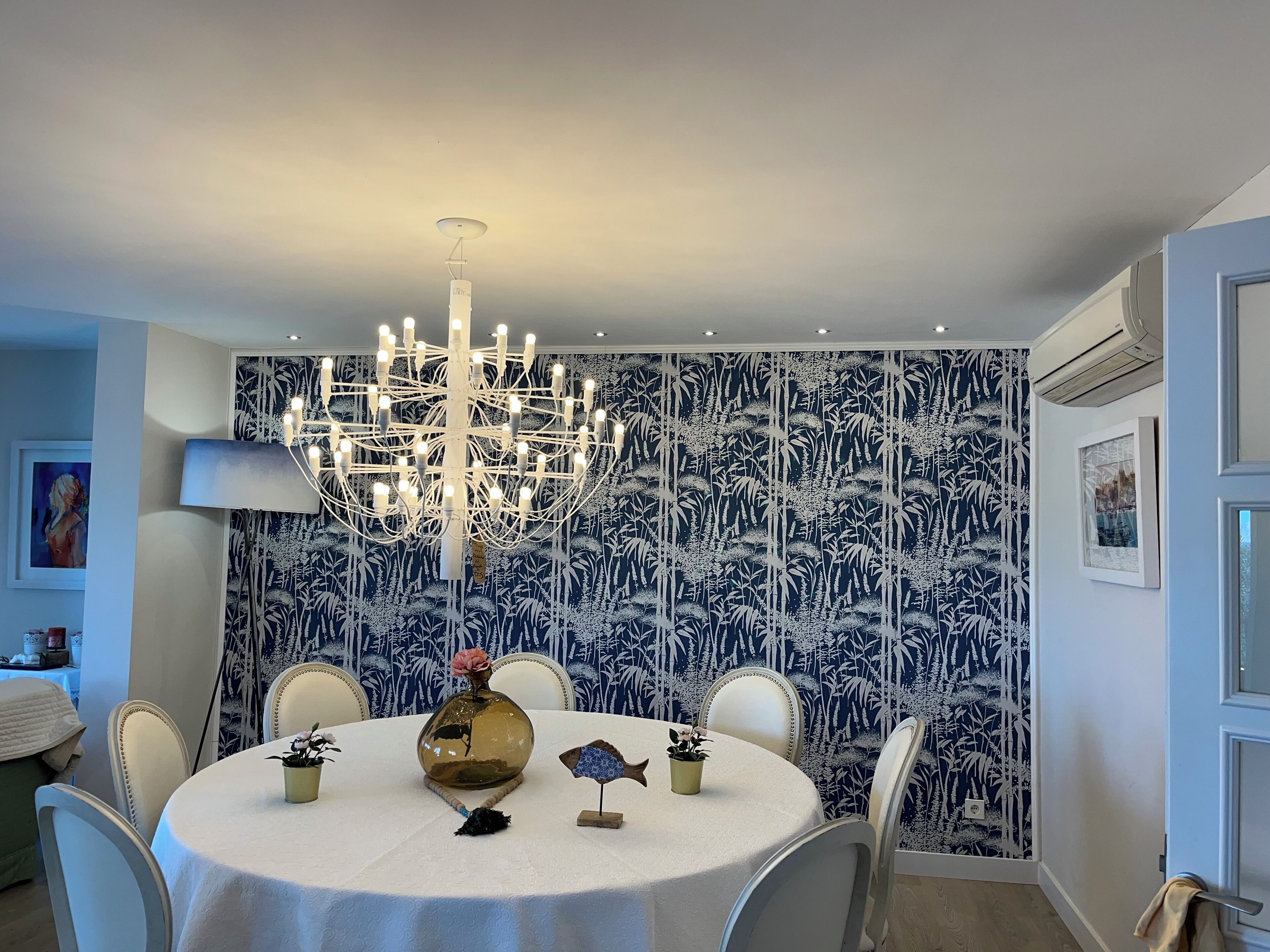 A dining area with a round table, chairs, a chandelier, and a wall with a blue and white pattern.