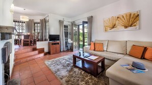 A living room with a sofa, coffee table, TV, and a dining area with chairs and a table. - Perfect Retreat Overlooking Pinhal Golf Course, Private pool, Off-street parking (Vilamoura)