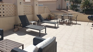 Une terrasse sur le toit, aménagée avec du mobilier d’extérieur, un barbecue et offrant une vue sur une colline.