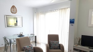 Un salon avec deux fauteuils, une table à manger en verre et un meuble pour la télévision.