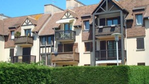 A row of townhouses with balconies, a clear blue sky, and a hedge in the foreground. - Cosy 3*** flat (Ouistreham)