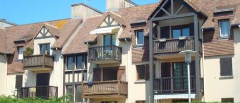 A row of townhouses with balconies, a clear blue sky, and a hedge in the foreground.