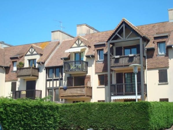 A row of townhouses with balconies, a clear blue sky, and a hedge in the foreground. - Cosy 3*** flat (Ouistreham)