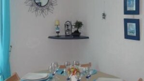 A dining area with a round table set for four, surrounded by wooden chairs with blue cushions. - Cosy 3*** flat (Ouistreham)