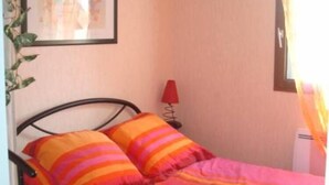 A bed with a colorful striped bedspread, a framed picture on the wall, a red lamp, and a window with curtains. - Cosy 3*** flat (Ouistreham)