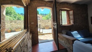 Habitación con paredes de piedra, un banco de madera, un sofá y grandes ventanales con vistas a la vegetación.