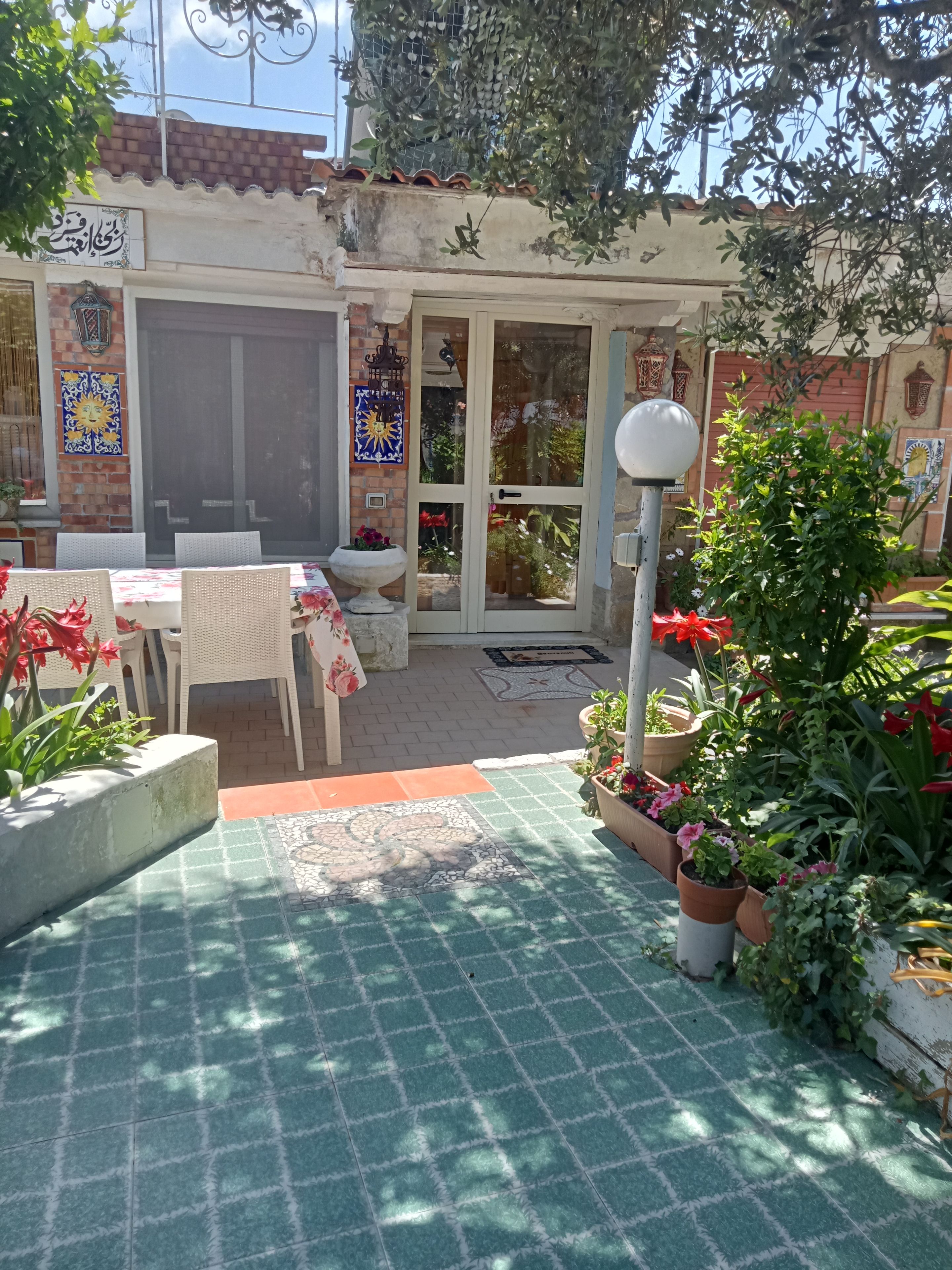 Eine Terrasse mit Tisch, Stühlen, einer Tür und Blumentöpfen.