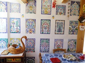 A room with a tiled wall featuring various colorful patterns, a wooden table with a swan-shaped tray, and a tablecloth with a floral design.