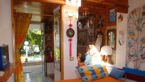 A room with a bed, a small table, and a chair. There is a window with curtains, a wall with various decorations, and a door leading outside. - Cleopatra: holiday home with terrace, Sorrento and Amalfi coast (Massa Lubrense)
