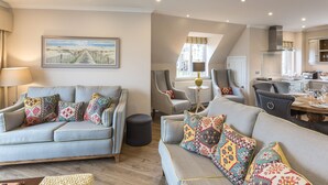 A modern living room with a sofa set, a dining table with chairs, and a kitchen area visible through an open door. - 1 Links Crescent 5 Star Selfcatering House Overlooking Old Course in St Andrews (St Andrews)