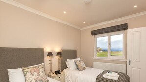 A bedroom with two beds, a window with a view, a bedside table with lamps, and a radiator. - 1 Links Crescent 5 Star Selfcatering House Overlooking Old Course in St Andrews (St Andrews)