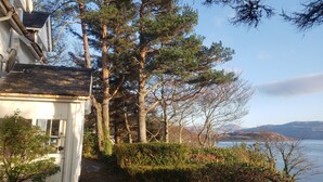 A house with a pathway leading to a lake, surrounded by trees and a clear sky. - Fabulous House with Stunning Sea Views to Skye. By NTS gardens. Great Privacy. (Kyle of Lochalsh)