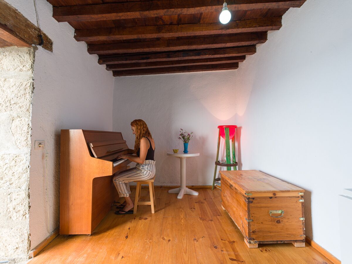 A room with a wooden piano, a small table with a vase, and a wooden chest.