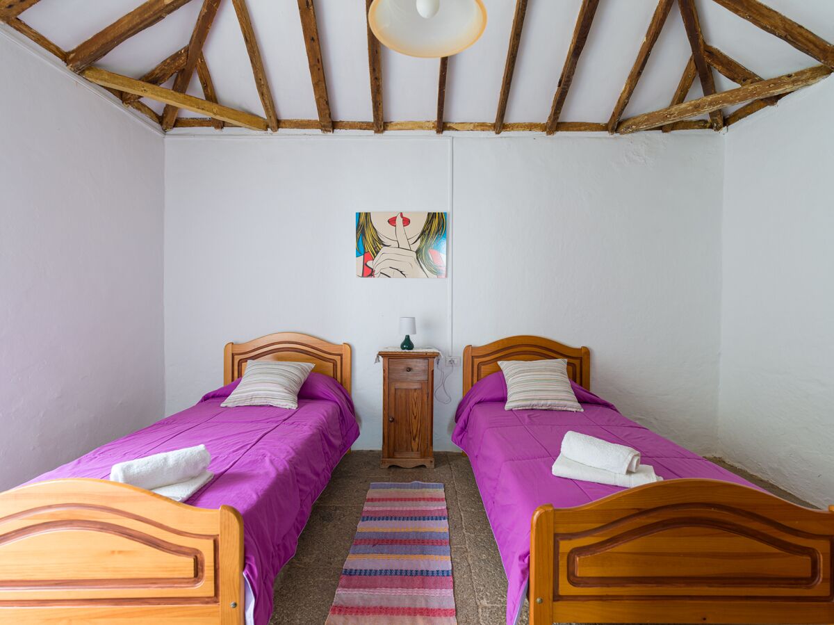 A bedroom with two wooden beds, a small wooden nightstand, a colorful striped rug, and a ceiling fan.