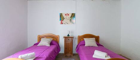 A bedroom with two wooden beds, a small wooden nightstand, a colorful striped rug, and a ceiling fan.