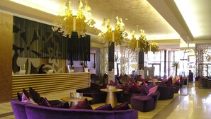 Eine großzügige Lobby mit violetten Sofas, einem Empfangstresen und aufwendigen Kronleuchtern.