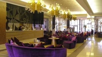 Eine großzügige Lobby mit violetten Sofas, einem Empfangstresen und aufwendigen Kronleuchtern.