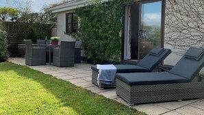 Un patio con mobiliario exterior, una puerta corrediza de vidrio y un jardín.
