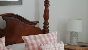 Una cama bien hecha con un cabecero de madera, almohadones a cuadros rosa y blanco, y una colcha blanca acolchada.