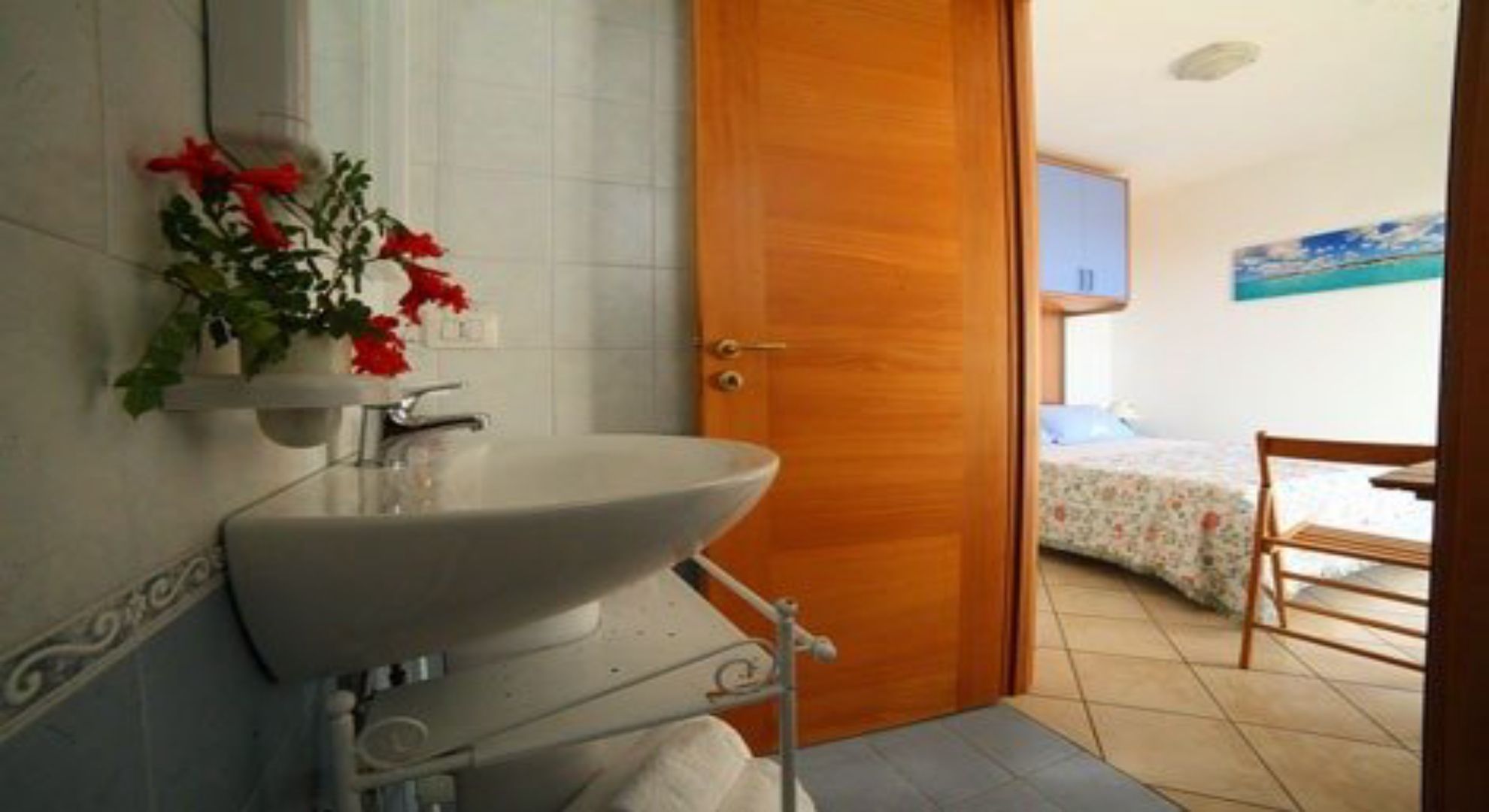 Ein Badezimmer mit Waschbecken, Spiegel und einer Tür zu einem Schlafzimmer mit Bett und Sessel.