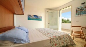 Una camera da letto con un letto, una sedia, una porta che dà su un balcone e un quadro appeso al muro.