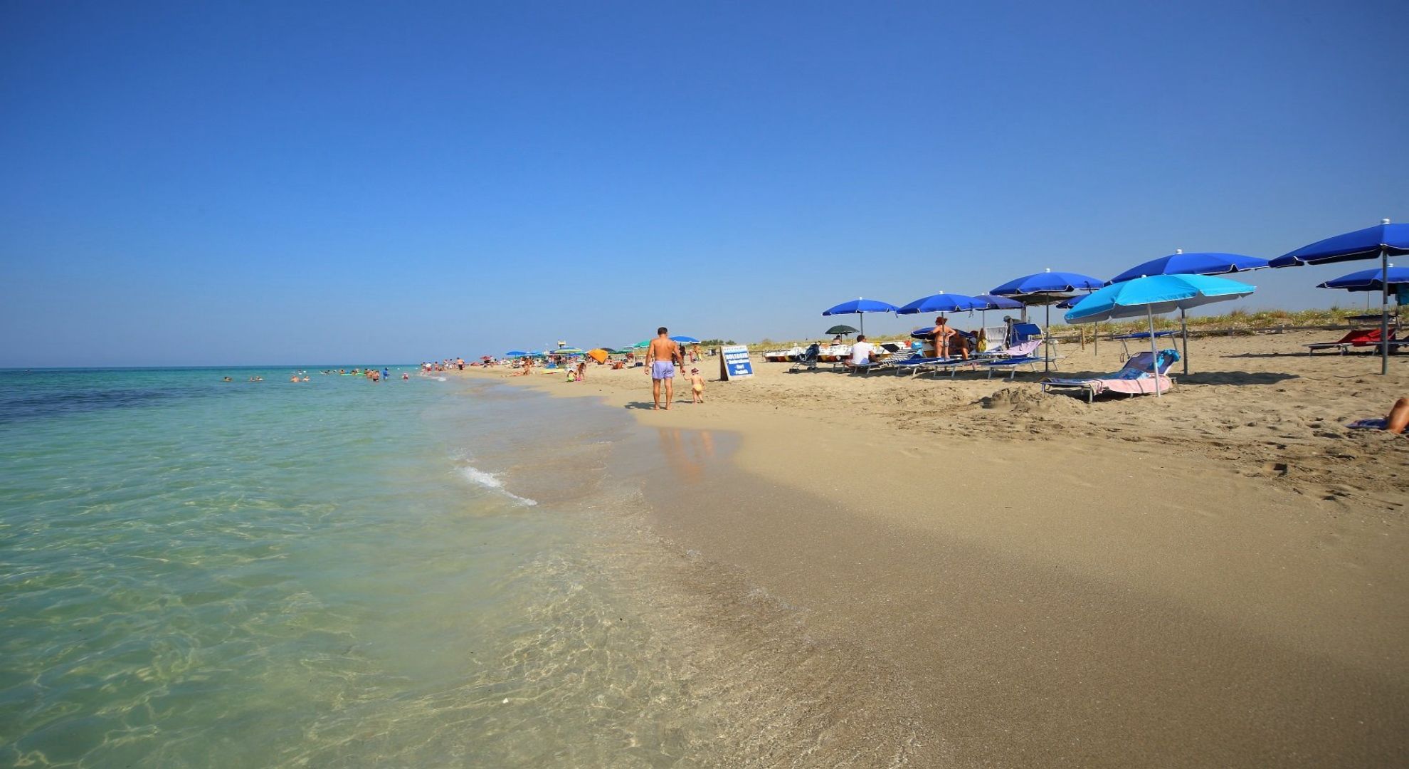 Ein Strand mit klarem Wasser, Liegestühlen und Sonnenschirmen.