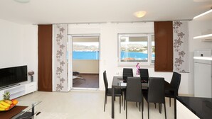 A modern living room with a flat-screen TV, a dining area with a table and chairs, and a kitchen area with a refrigerator. - Apartment Palm Beach 2 for 6-8 persons - Amazing beach house rental! (Okrug Gornji)