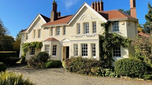 A large, two-story house with a symmetrical facade, multiple chimneys, and a gravel driveway. - Manor house set in five acres of gardens with private golf course, near Ludlow. (Ludlow)