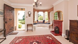 A spacious living room with a large red rug, a fireplace, and a bay window with blue cushions. - Manor house set in five acres of gardens with private golf course, near Ludlow. (Ludlow)