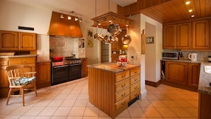 A kitchen with wooden cabinets, a central island with drawers, a hanging pot rack, and a microwave. - Manor house set in five acres of gardens with private golf course, near Ludlow. (Ludlow)
