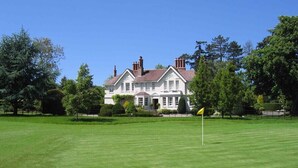 A large, white, two-story house with a red roof, surrounded by a well-maintained lawn and trees. - Manor house set in five acres of gardens with private golf course, near Ludlow. (Ludlow)