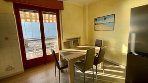 Uma sala de jantar com mesa e cadeiras, geladeira e vista para o mar através de uma porta de correr.