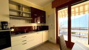 Cozinha moderna com armários brancos, bancada preta e vista para uma varanda com grade.