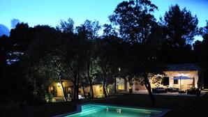 A nighttime view of a residential property with a swimming pool, outdoor seating area, and a well-lit patio.