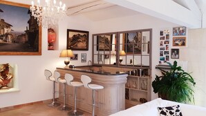 A modern kitchen with a bar area, bar stools, a chandelier, and various framed artworks on the walls.