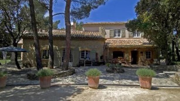 A rustic stone building with a tiled roof, surrounded by trees and potted plants.