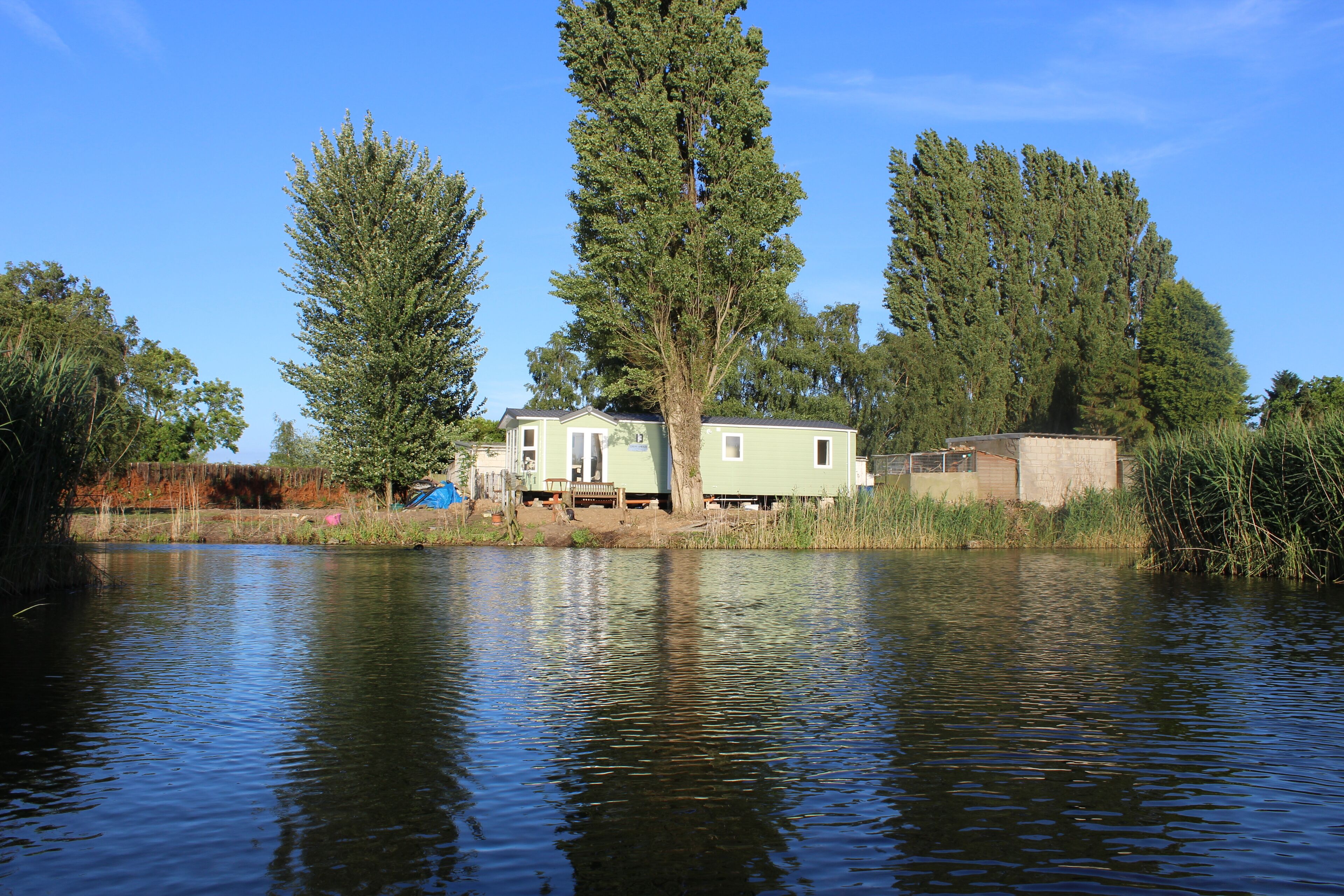 Un chalet au bord du lac, doté d’un quai, entouré de grands arbres et surplombant un ciel dégagé.