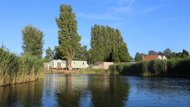A lakeside property with a small cabin and a larger house, surrounded by tall trees and a calm water body. - MARSHLANDS LAKESIDE NATURE RETREAT (Barton-upon-Humber)