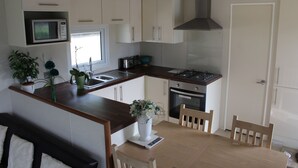 A compact kitchen with white cabinets, a microwave, a stove, and a sink. There is a dining table with chairs and a potted plant on the counter. - MARSHLANDS LAKESIDE NATURE RETREAT (Barton-upon-Humber)