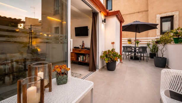 A balcony with a table, chairs, potted plants, a TV, and a bookshelf.